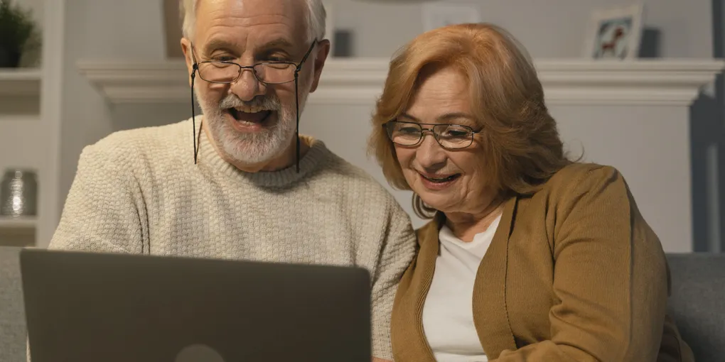 Un couple de seniors découvre des photos sur un écran, l'air joyeux et surpris